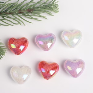 May include: Six iridescent heart-shaped beads with a lace pattern. The beads are in shades of red, pink, and white.