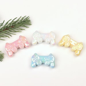 May include: Three iridescent plastic game controller charms in pink, blue, and yellow. The charms are shaped like a video game controller and have a pearlescent finish.