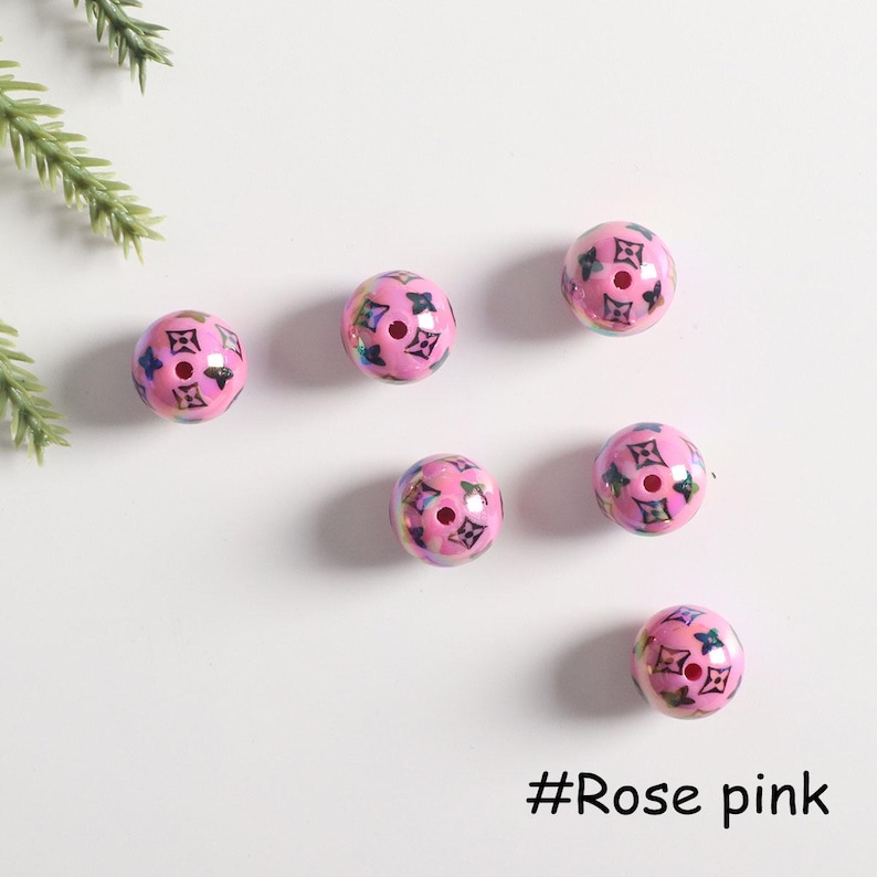 May include: Six pink round beads with a black and white pattern. The beads have a hole in the center and are scattered on a white surface. #Rose pink