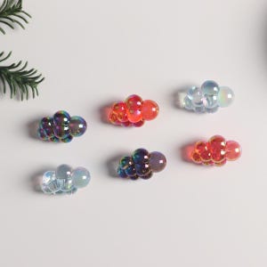 May include: Six iridescent grape clusters in various colors, including blue, red, and purple. The grapes are made of glass and have a shiny, reflective finish.