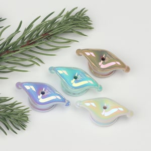 May include: Four iridescent glass beads in different colours: light brown, light blue, light purple, and white. Each bead has a hole in the centre and a unique, slightly wavy shape.