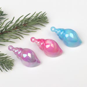 May include: Three iridescent seashell ornaments in blue, pink, and purple. Each seashell has a gold loop for hanging.