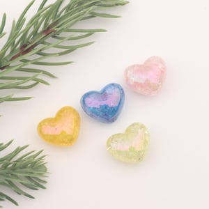 Könnte beinhalten: Vier regenbogenfarbene herzförmige Glasornamente in Rosa, Blau, Gelb und Grün.