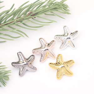 Puede incluir: Cuatro abalorios de estrella de mar en diferentes acabados metálicos: plata, oro rosa, oro y plata oscura. Los abalorios son todos del mismo tamaño y forma, con un diseño de estrella de cinco puntas.