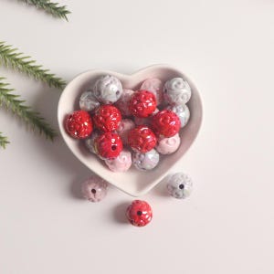 May include: A heart-shaped bowl filled with red, pink, and white ceramic beads. The beads have a swirl design.