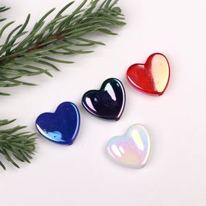 Puede incluir: Cuatro cuentas iridiscentes en forma de corazón en rojo, azul, morado y blanco.