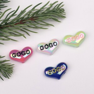 以下が含まれることがあります： 「GOGO」と書いてある虹色のハート型のチャームが4つ。ハートはピンク、白、緑、青です。