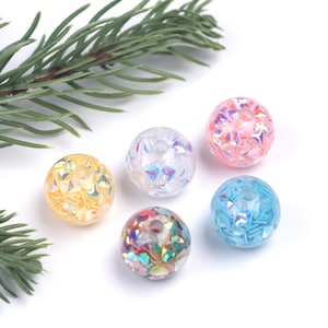 Puede incluir: Cinco cuentas redondas iridiscentes de varios colores, incluyendo rosa, azul, amarillo, transparente y multicolor. Las cuentas están hechas de vidrio y tienen un acabado brillante.
