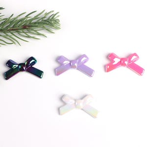 May include: Four iridescent plastic bows in different colors: black, purple, pink, and white. The bows are arranged in a row on a white background.