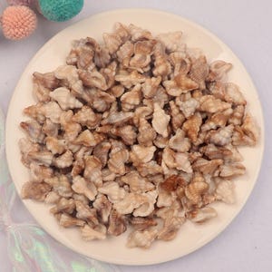 May include: A collection of small, beige and brown seashells arranged on a white plate. The shells have a spiral shape and varying shades of brown and beige. The plate is round and has a slightly raised edge. The shells are likely for crafting or decorative purposes.