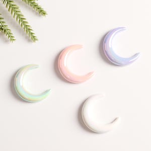 Puede incluir: Cuatro adornos de cerámica en forma de media luna iridiscente en rosa, blanco y azul.