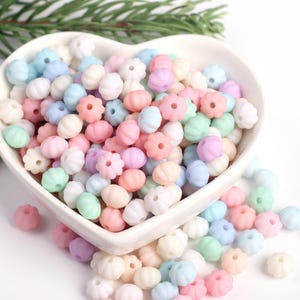 May include: A bowl filled with pastel-colored plastic beads. The beads are shaped like small pumpkins with a flower design on the top.