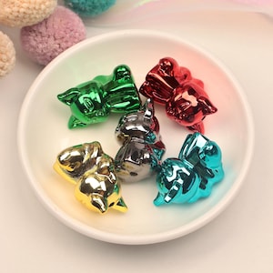 May include: A collection of colorful, metallic animal figurines in a white bowl. The figurines are in various colors, including green, red, gold, silver, and teal. The figurines are small and appear to be made of a shiny material.