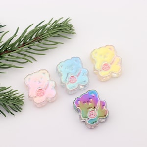 Puede incluir: Cuatro abalorios de oso de vidrio iridiscente en rosa, azul, amarillo y morado. Cada abalorio de oso tiene un pequeño corazón rosa en el pecho.