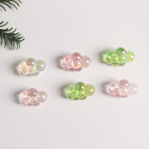 Op de afbeelding: Zes iriserende haarclips in de vorm van een wolk. De clips zijn gemaakt van helder plastic met een parelmoer afwerking. Er zijn twee roze clips, twee groene clips en twee heldere clips.