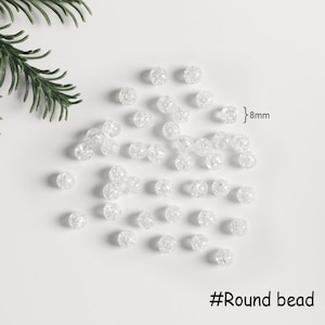 May include: A close-up of a pile of clear round beads with a textured surface. The beads are 8mm in diameter. #Round bead