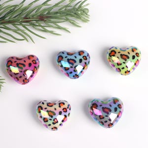 May include: Five iridescent heart-shaped beads with a leopard print design. The beads are in shades of pink, blue, green, and yellow.