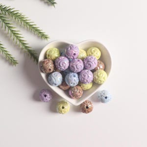 May include: A heart-shaped bowl filled with pastel-colored ceramic beads. The beads have a swirl design and come in shades of purple, yellow, and brown.