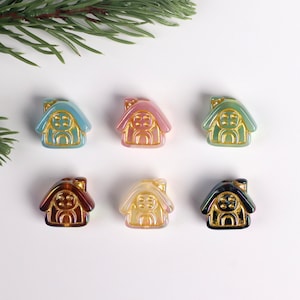 May include: Six iridescent glass house-shaped beads with gold accents. The beads are in various colours, including blue, pink, yellow, brown, and black.