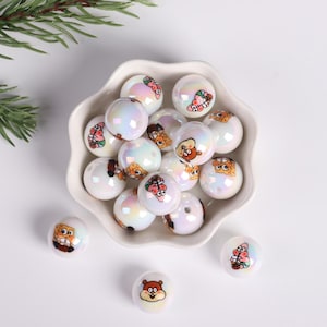May include: A white bowl filled with iridescent white beads with cartoon character images. The beads are scattered around the bowl on a white surface.