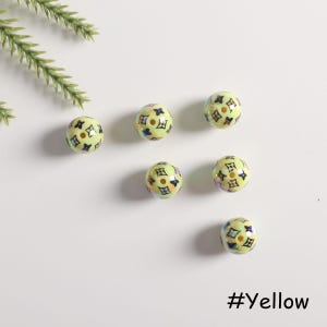 May include: Six yellow round beads with a black and white pattern. The beads have a glossy finish and are scattered on a white surface. #Yellow
