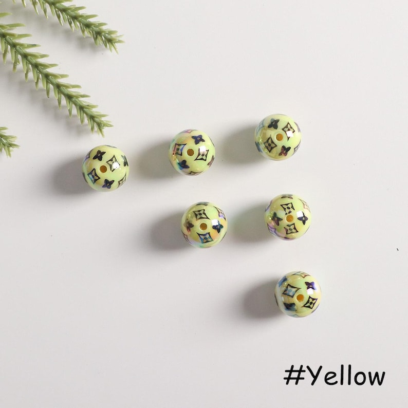 May include: Six yellow round beads with a black and white pattern. The beads have a glossy finish and are scattered on a white surface. #Yellow