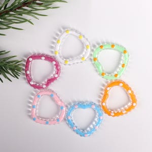 May include: Six heart-shaped glass rings with colorful polka dots. The rings are in shades of pink, blue, green, orange, and white.