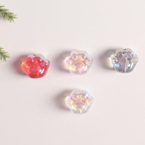 May include: Four iridescent glass paw print charms. Three are clear with a rainbow sheen, and one is red with a rainbow sheen.