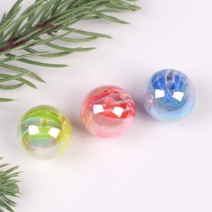 May include: Three iridescent glass beads with a swirl pattern. The beads are in shades of blue, pink, and green.