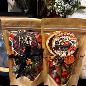 May include: Two brown paper pouches containing dried botanical simmer pot ingredients. The left pouch features a black label reading Haunted Harvest, while the right pouch has a round label reading Pumpkin Season Simmer Pot with a black cat illustration.