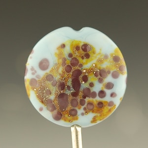 May include: A light blue glass bead with brown and gold speckles. The bead has a mottled, speckled appearance.