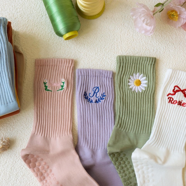 May include: A collection of ribbed crew socks in various pastel colors, each embroidered with unique designs. The socks include text that says "The Coastal Club" and the name "Rosie". Other designs include a daisy, a letter "R", and a floral design.