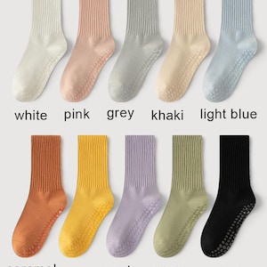 May include: A collection of ten pairs of socks in various colors, including white, pink, grey, khaki, and light blue. The socks have ribbed cuffs and dotted grips on the soles. Additional colors are caramel, yellow, purple, green, and black. The names of the colors are printed below each pair.