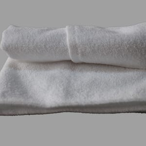 May include: Two white towels folded on top of each other. The top towel is rolled up and the bottom towel is flat.