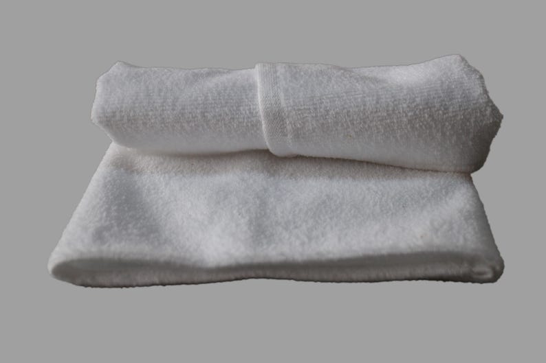 May include: Two white towels folded on top of each other. The top towel is rolled up and the bottom towel is flat.