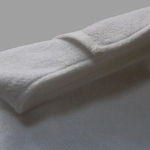 May include: A white bath towel folded in half, with the top layer folded over to create a smooth, flat surface.