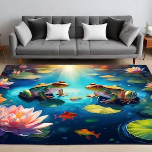 Op de afbeelding: Een blauw en groen vloerkleed met een vijverscène met twee kikkers, waterlelies en bloemen. Het vloerkleed heeft een helder, kleurrijk ontwerp.
