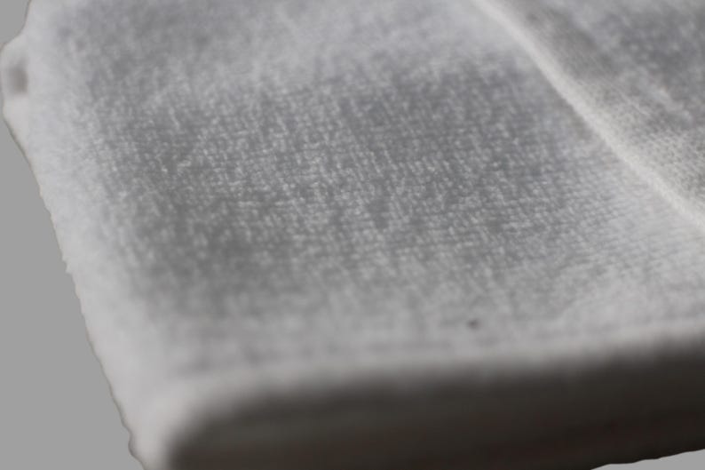 May include: Close-up of a white, soft, and textured fabric. The fabric has a smooth, even surface with a subtle sheen.