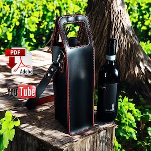 May include: A black leather wine bottle carrier with red stitching and a shoulder strap. A full bottle of red wine sits next to the carrier. The carrier has a handle at the top and is on a wooden surface.