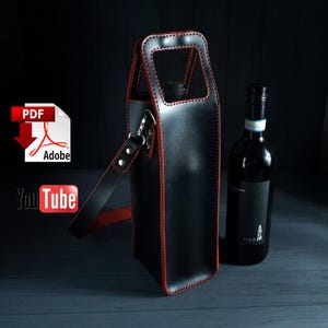 May include: Black leather wine bottle carrier with a red stitched trim and a long adjustable strap. The carrier has a top handle and is designed to hold a standard size wine bottle.