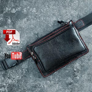 Puede incluir: Riñonera de cuero negro con costuras rojas. La riñonera tiene un compartimento principal rectangular y un bolsillo delantero más pequeño, ambos con cremalleras. La correa ajustable tiene una hebilla de plástico negro. Logotipos de Adobe PDF y YouTube visibles.