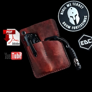 May include: A brown leather pocket organiser with two pockets for carrying small items. The organiser has a stitched edge and is shown with a black pocket knife and a black and white patch with the text "EDC".