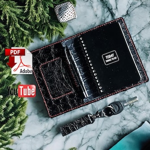 May include: Black leather wallet with red stitching detail. The wallet has a built-in notebook with the words "Today Things To Do" on the cover. A key chain with a key is attached to the wallet.