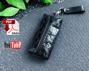 May include: Black leather key pouch with a textured crocodile pattern, a zipper closure, and a small leather strap with a metal clasp. The pouch is rectangular and appears to be made of high-quality leather.