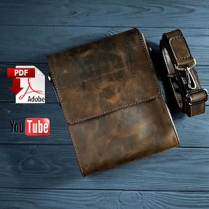 May include: A brown leather crossbody bag with a flap closure and adjustable strap. The bag has a distressed finish, and the strap features metal hardware. The bag is shown on a dark blue wooden surface.