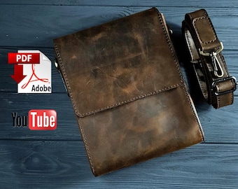 May include: A brown leather crossbody bag with a flap closure and adjustable strap. The bag has a distressed finish, and the strap features metal hardware. The bag is shown on a dark blue wooden surface.