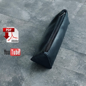 May include: A black leather pencil case with a zipper closure. The case is triangular in shape and appears to be handmade. The Adobe PDF and YouTube logos are visible in the background.