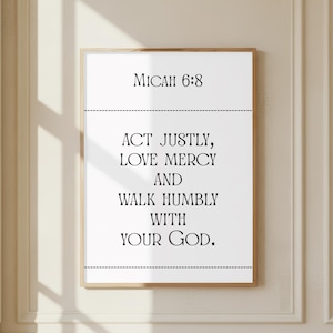 May include: A framed print with the text "Micah 6:8" at the top, followed by the words "Act Justly, Love Mercy, And Walk Humbly With Your God." The text is in a black, serif font on a white background, framed in a light brown wooden frame.