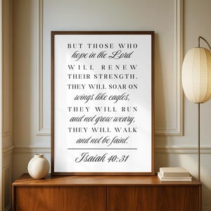 Könnte beinhalten: Ein gerahmter Druck mit dem Text "BUT THOSE WHO hope in the Lord...Isaiah 40:31" in schwarzer Schrift. Der Druck befindet sich in einem dunkelbraunen Rahmen und wird auf einem Holzschrank ausgestellt. Eine weiße Vase und eine Lampe mit Papierschirm sind ebenfalls zu sehen.