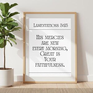 May include: A framed print with the text "Lamentations 3:23: His mercies are new every morning, great is your faithfulness." The print is in a light wood frame and is displayed on a wall next to a potted plant.